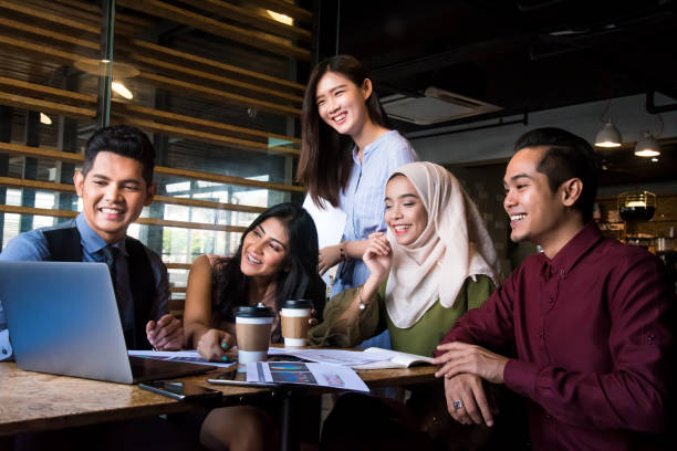 Multi-ethnic team discussion using laptop and digital tablet for online marketing analyzing, business strategic planning, online video conferencing and leadership training.